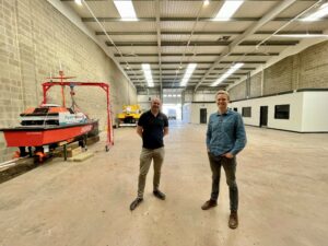 Two men standing in a ware house next to an Uncrewed Surface Vessel